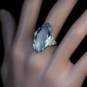 Detalle de un anillo ovalado de cristal azul con diamantes laterales en un dedo