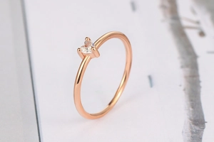 Vista macro di un anello sottile in oro rosa con zircone a cuore e fascia lucida