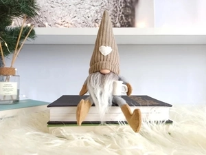 Knitted faceless Christmas gnome sitting on books with pine branches for home decor