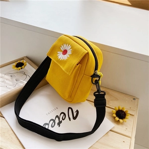 Yellow canvas crossbody bag with daisy embroidery on a wooden table, minimalist style
