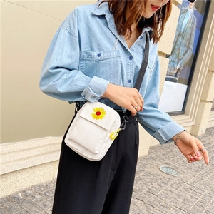 Detail of white canvas crossbody bag featuring daisy embroidery and yellow ring zipper
