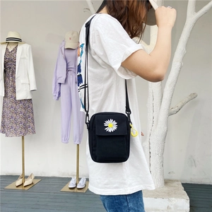 Detailed view of daisy embroidery on a black canvas crossbody bag worn by a model