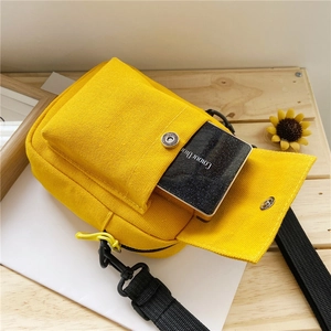 Detail of yellow canvas crossbody bag with magnetic pocket on a light wooden surface
