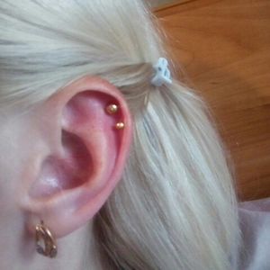 Close-up of golden stainless steel ball earrings and hoop on earlobe for piercing show