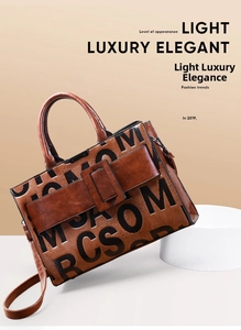 Detail of brown leather tote bag featuring debossed letters and a wide buckle strap