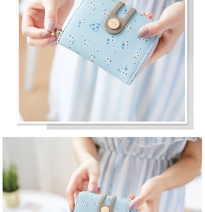 Detail of light blue floral wallet with buckle and zipper held by a model in soft light