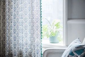 Detail of white curtain with blue vintage print and green tassel fringe in a cozy room