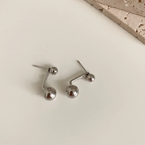 Macro shot of minimalist silver ball stud earrings on a textured cream background