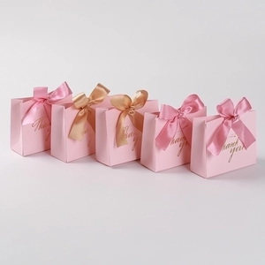 Detailed view of pink paper wedding gift bags with gold Thank You text and ribbons