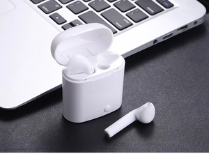 Primer plano de auriculares TWS blancos con estuche de carga sobre teclado de un portátil
