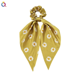 Detail of yellow satin scrunchie featuring white daisy patterns and long ribbons