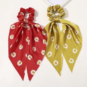 Detail of red and yellow satin daisy print scrunchies with elegant long ribbon streamers