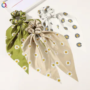 Detail of three satin scrunchies with long ribbons and daisy floral prints in soft colors