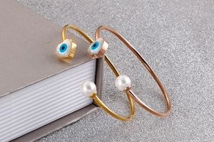 Detail of open gold and rose gold bangles with heart evil eye charms and white pearls