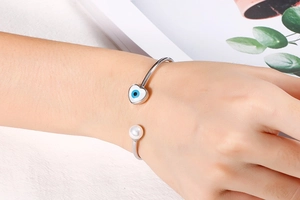 Detail of silver C-shaped cuff bracelet with white pearl and heart-shaped evil eye motif