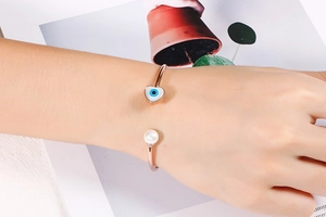 Detail of rose gold evil eye heart bracelet with pearl on a female wrist