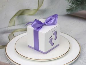 Detail of laser-cut baby footprint design on white gift box with purple silk ribbon