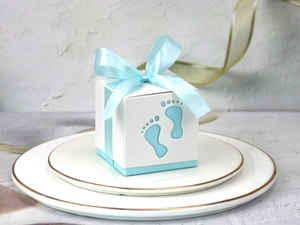 Detail of laser-cut baby footprint gift box with blue satin ribbon on ceramic plate