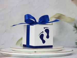 Detail view of hollow baby footprint candy box with royal blue ribbon on a white plate