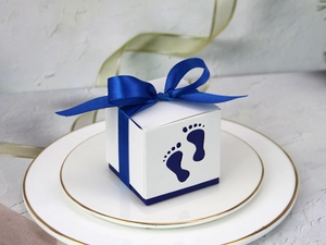 Detail of white hollow baby footprint candy box with dark blue ribbon on porcelain plate