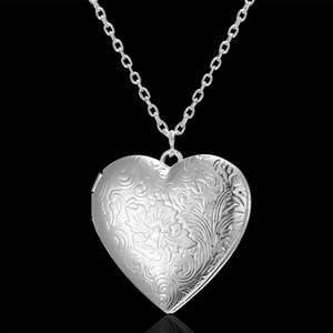 Detailed macro view of an engraved silver heart locket pendant with floral patterns