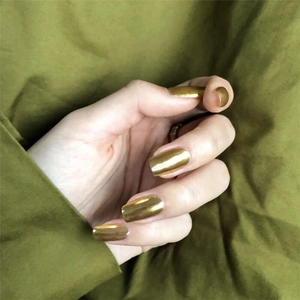 Glossy golden mirror finish medium long press-on nails shown on hand with green background