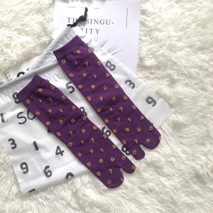 Close-up of purple Tabi split-toe socks with golden numeral knit patterns and ribbed cuffs