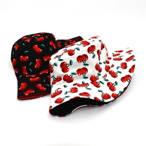 Détail de deux bobs réversibles avec motifs cerises rouges en toile noire et blanche