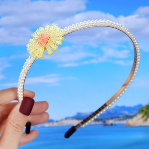Detail of handmade pearl headband with yellow beaded daisy flowers against a beach background