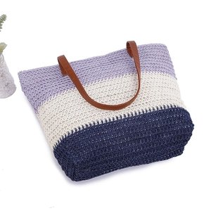 Detail of tricolor woven beach tote featuring purple, beige, and navy with leather handles