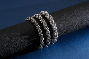 Close-up of three widths of silver Byzantine chain bracelets on a black display stand
