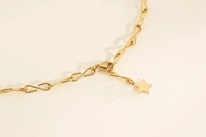 Makroaufnahme einer goldenen S-Gliederkette mit filigranem Sternanhänger auf beigem Hintergrund