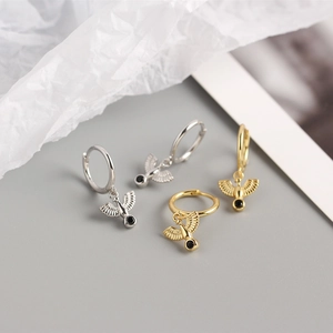 Detail of silver and gold hoop earrings featuring bird charms with black gemstones