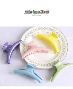 Detail of five candy-colored large matte hair claws on a white minimalist plate