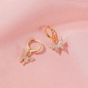 Vue détaillée de boucles d'oreilles papillon dorées serties de zircons sur tissu rose