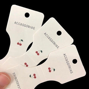White cherry print cardboard tags for hair accessories and necklaces in a stacked display