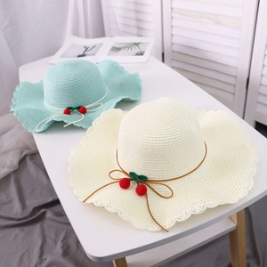 Detail of straw sun hats in mint green and beige with cherry and bow accents