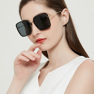 Close-up of model wearing black oversized square sunglasses with gold metal temples