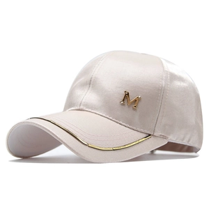 Close-up of satin champagne baseball cap with golden M letter and metallic brim detail