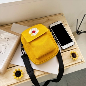 Detail of yellow canvas crossbody bag featuring embroidered daisy on a wooden surface