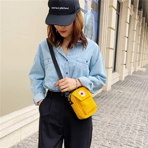 Outdoor shot of yellow canvas mini crossbody bag with daisy embroidery detail