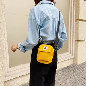 Side view of a yellow canvas crossbody bag with daisy embroidery worn by a model