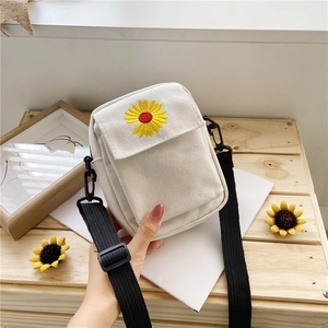 Detailed embroidery of a yellow daisy on a cream canvas mini crossbody bag