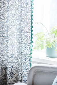 Detail of linen texture curtain with blue floral print and decorative green tassel trim