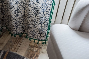 Close-up of beige curtain with blue retro floral pattern and green tassel fringe detail