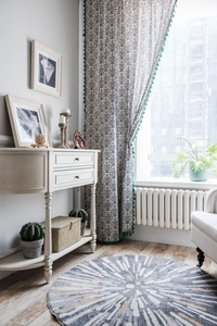Detail of blue pattern curtain with green tassels and a white drawer side cabinet