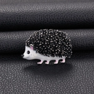 Cute cartoon hedgehog enamel brooch with black quills and pink feet on leather background