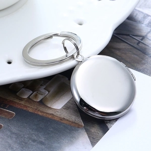 Polished stainless steel round locket keychain displayed on a white ceramic plate