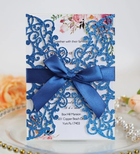 Close-up of blue glitter laser-cut wedding invitation with elegant satin ribbon bow