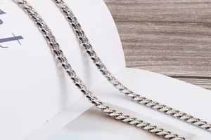 Detailed view of polished silver NK chain body link over a book and wooden background